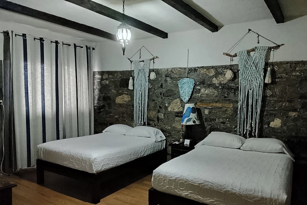 Ein Zimmer mit zwei Betten, einer Steinsäule, Holzboden und einer hängenden Leuchte.