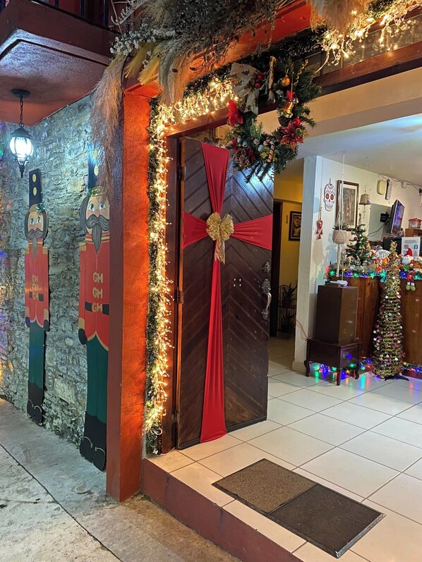 A decorated entrance with a wooden door, festive lights, and a Christmas tree inside. - Grann Posada Xilitla (Xilitla)