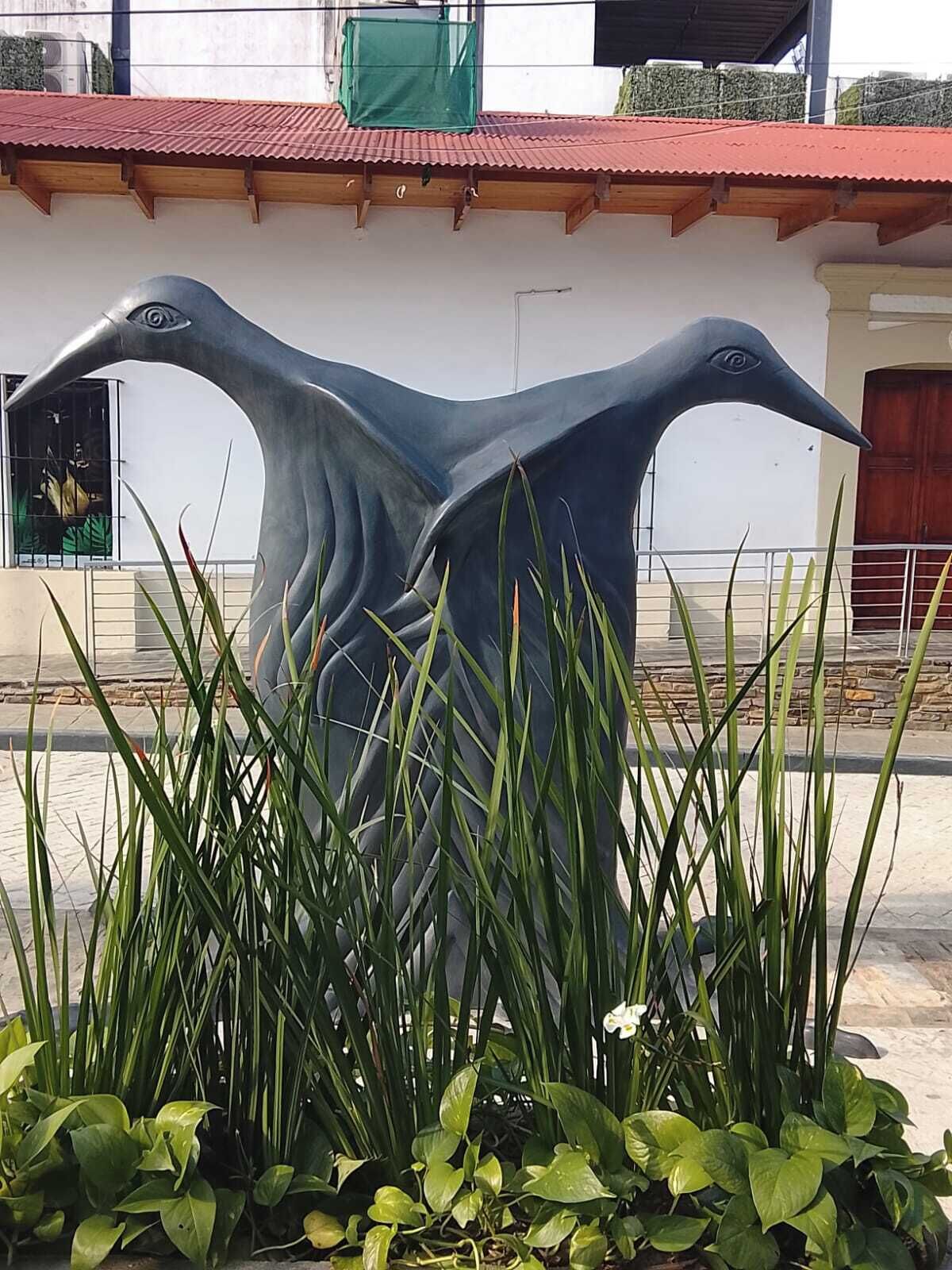 A sculpture of two birds in a garden area with plants in the foreground.