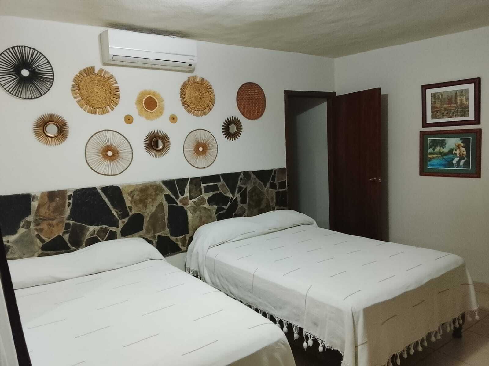 A room with two beds, a stone headboard, decorative wall art, and an air conditioning unit.