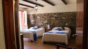 A room with two beds, a stone wall, wooden beams, and a small table with a lamp. - Grann Posada Xilitla (Xilitla)
