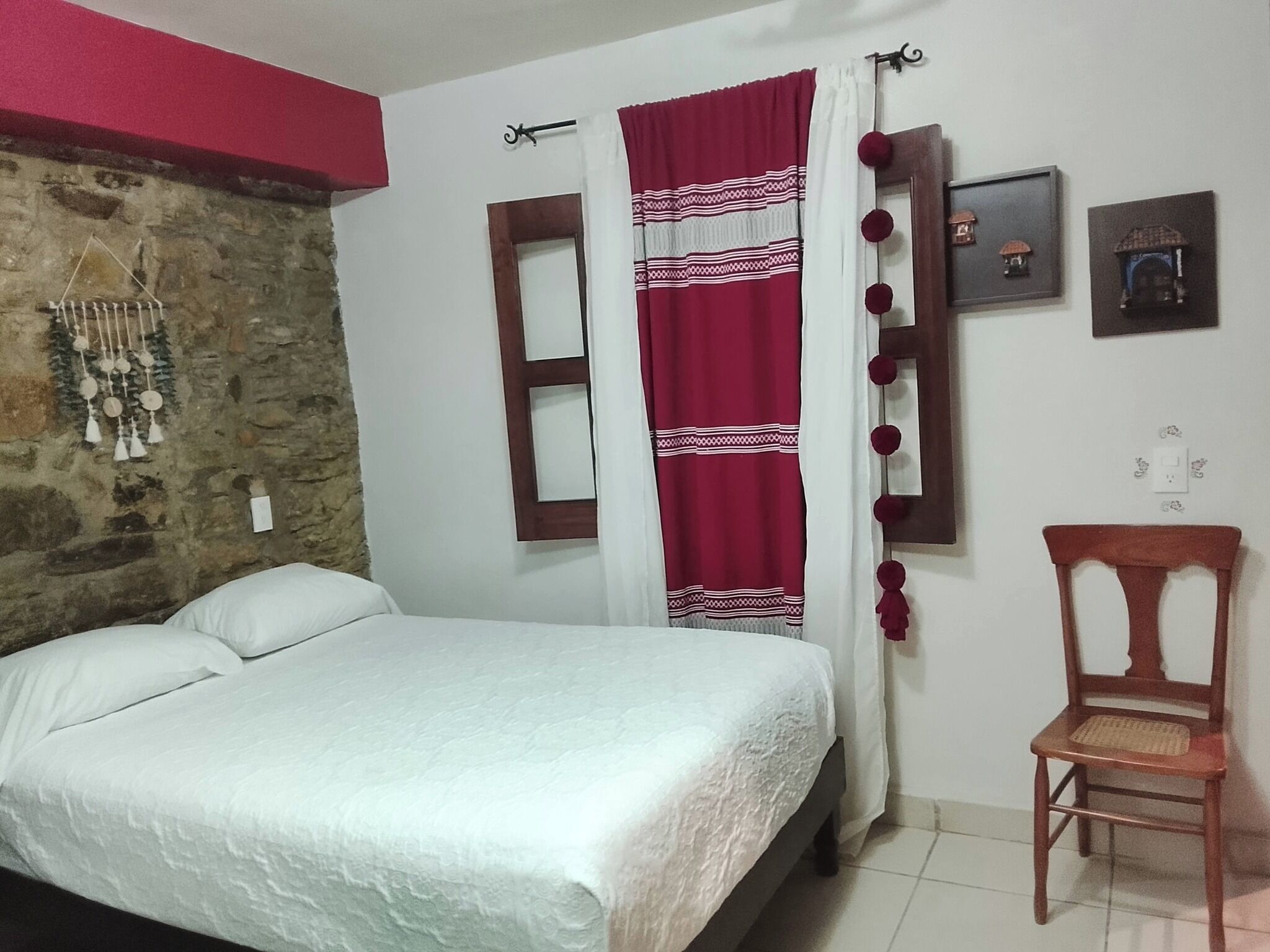 A bedroom with a bed, a chair, a stone wall, and a window with curtains.