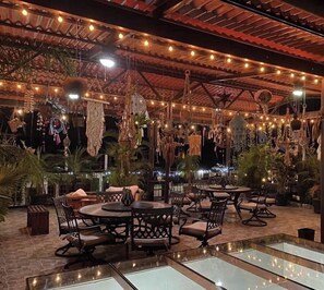 An outdoor dining area with round tables and chairs, surrounded by hanging decorations and string lights. - Grann Posada Xilitla (Xilitla)