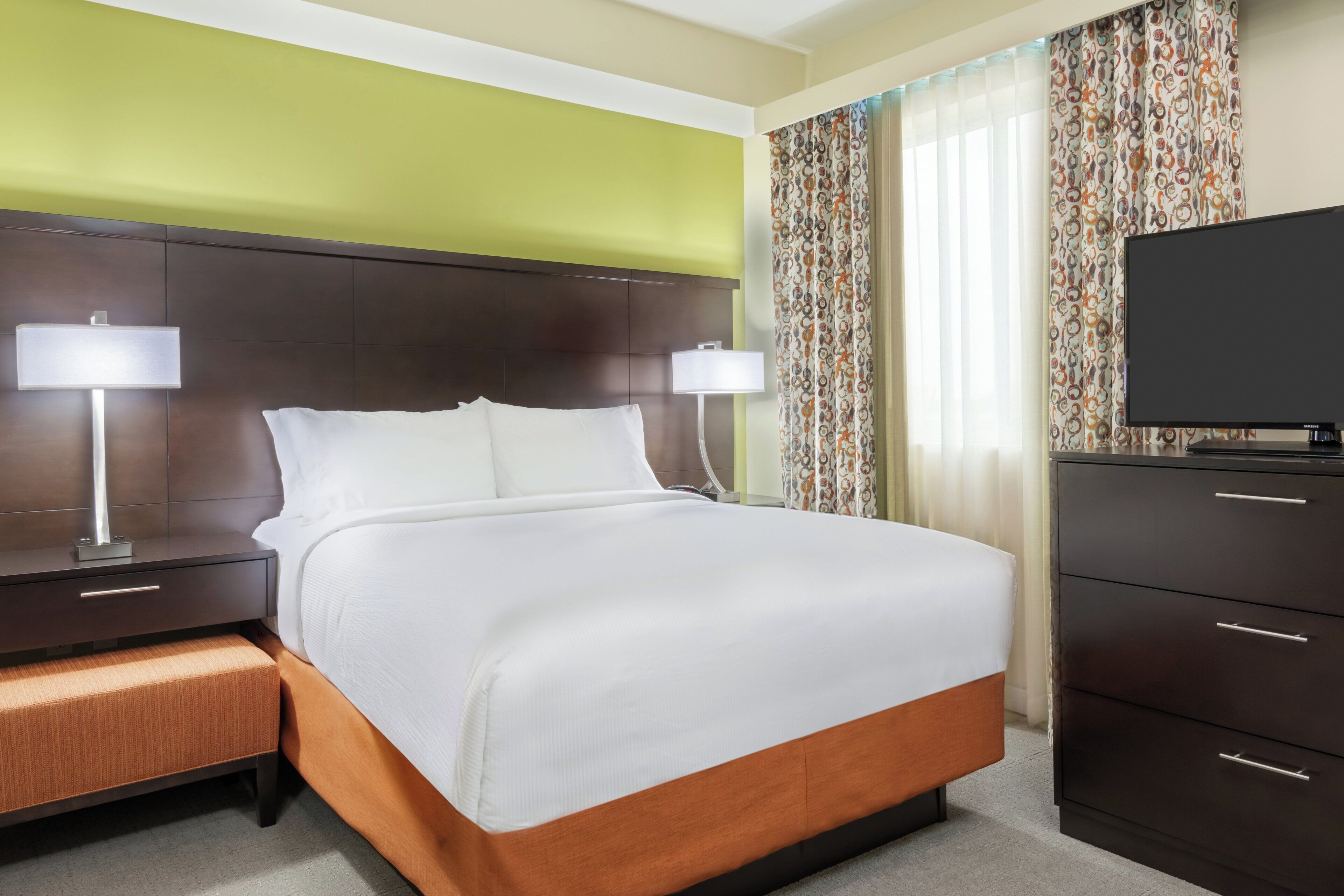 A hotel room with a large bed, two bedside tables with lamps, a dresser, and a television.