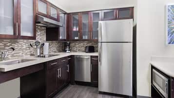 A modern kitchen with dark wooden cabinets, a stainless steel refrigerator, a dishwasher, and a tiled backsplash.