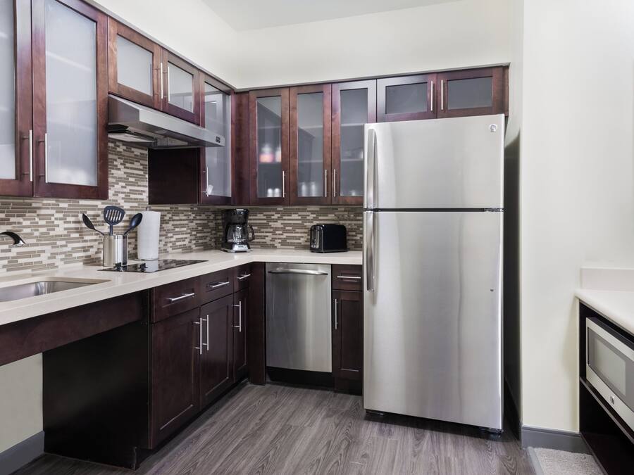 A modern kitchen with dark wooden cabinets, a stainless steel refrigerator, a dishwasher, and a tiled backsplash.