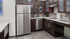 Una cocina moderna con electrodomésticos de acero inoxidable, armarios de madera oscura, un salpicadero de azulejos y un lavavajillas integrado.