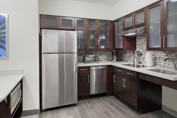 Una cocina moderna con electrodomésticos de acero inoxidable, armarios de madera oscura, un salpicadero de azulejos y un lavavajillas integrado.