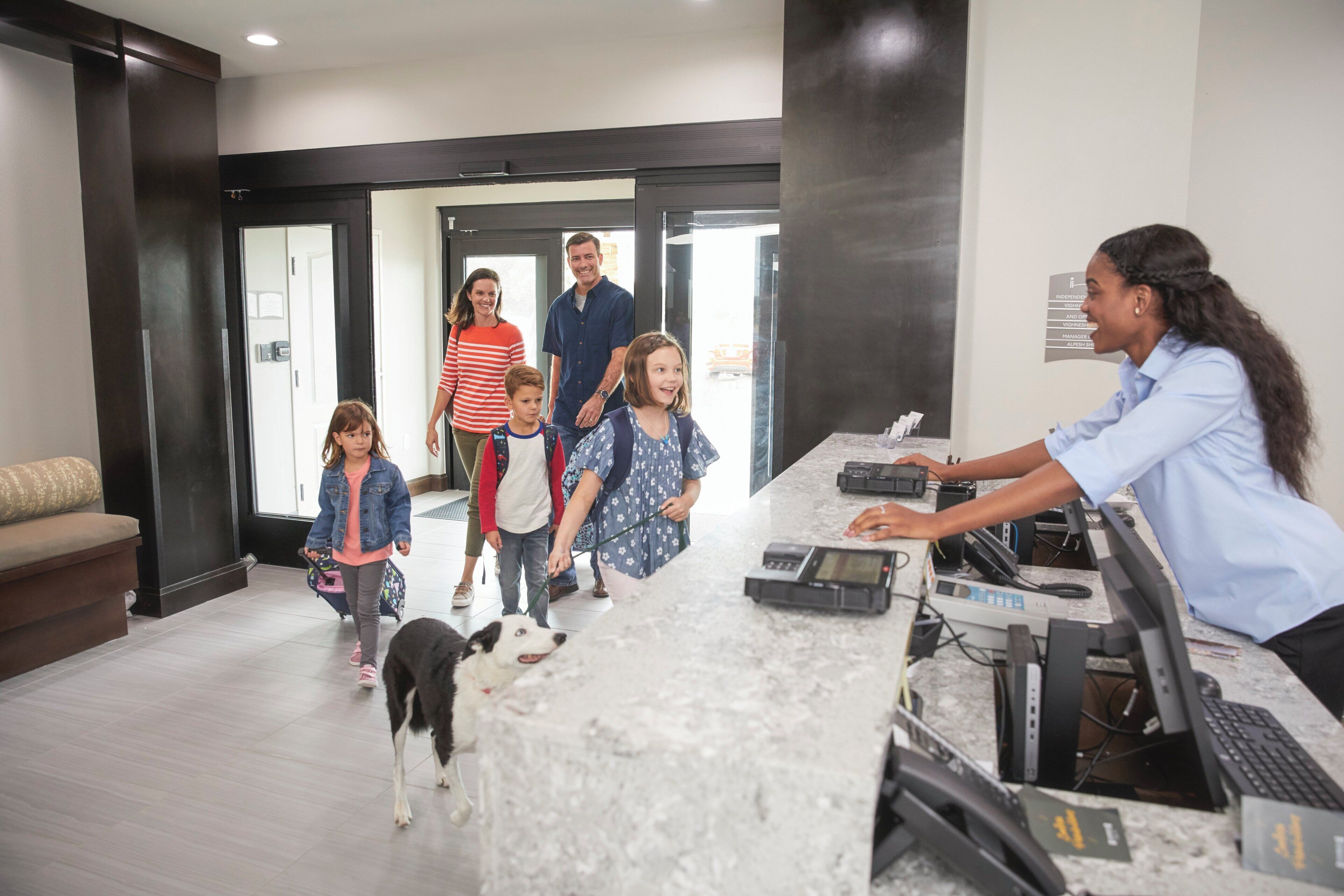 A reception desk with a receptionist, a family with children, and a dog walking through a lobby with a modern interior.