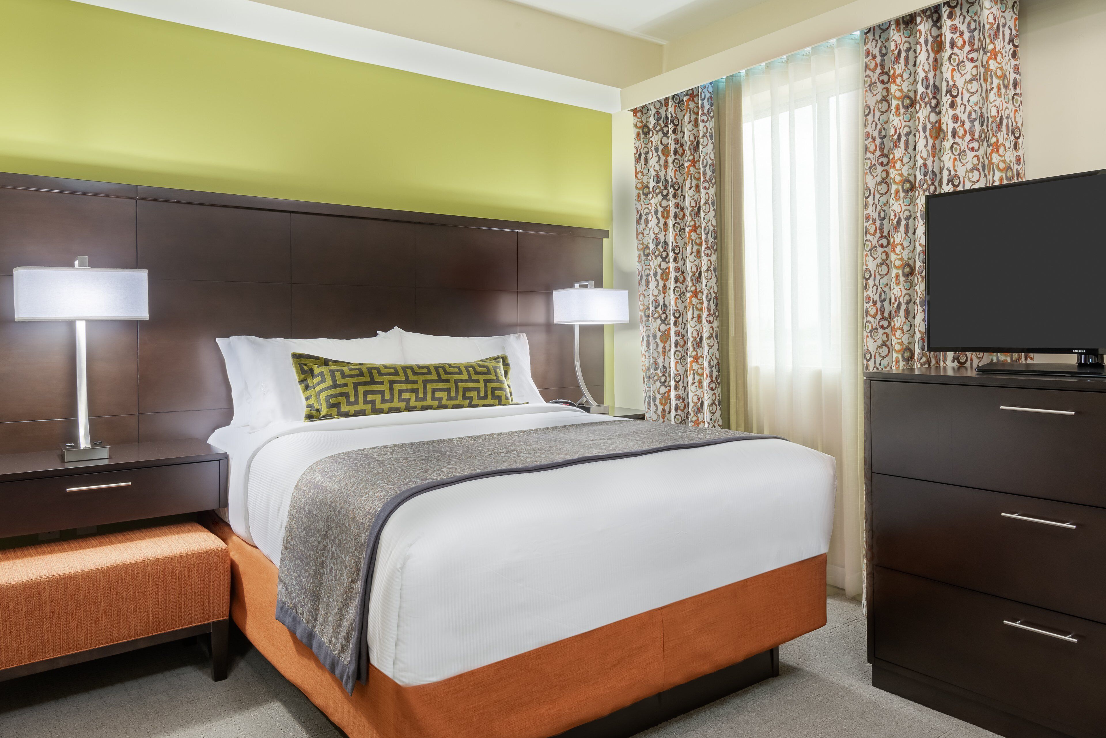 A hotel room with a bed, bedside lamps, a television, and a dresser.