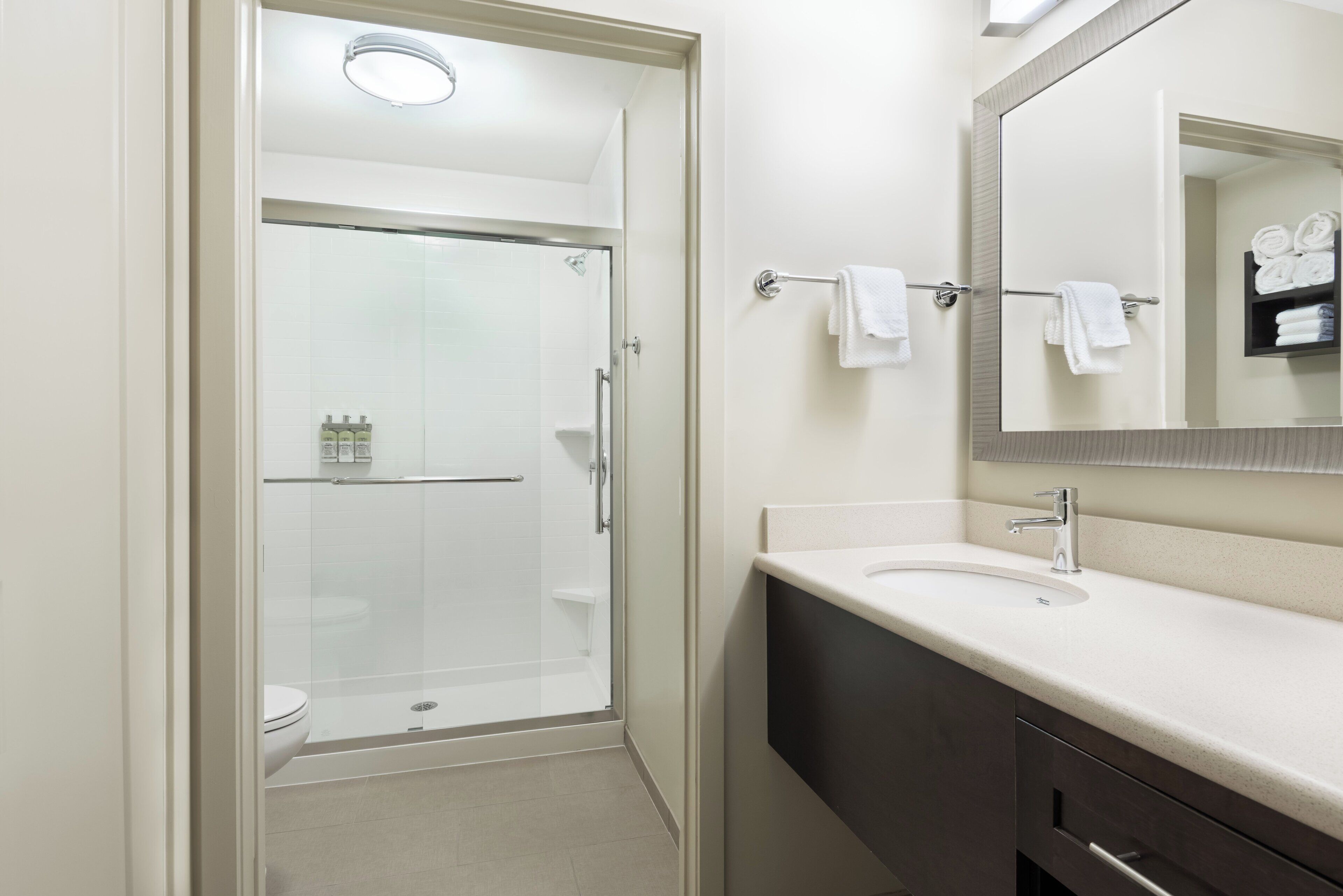 A modern bathroom with a glass-enclosed shower, a white sink with a mirror above it, and a towel rack with folded towels.