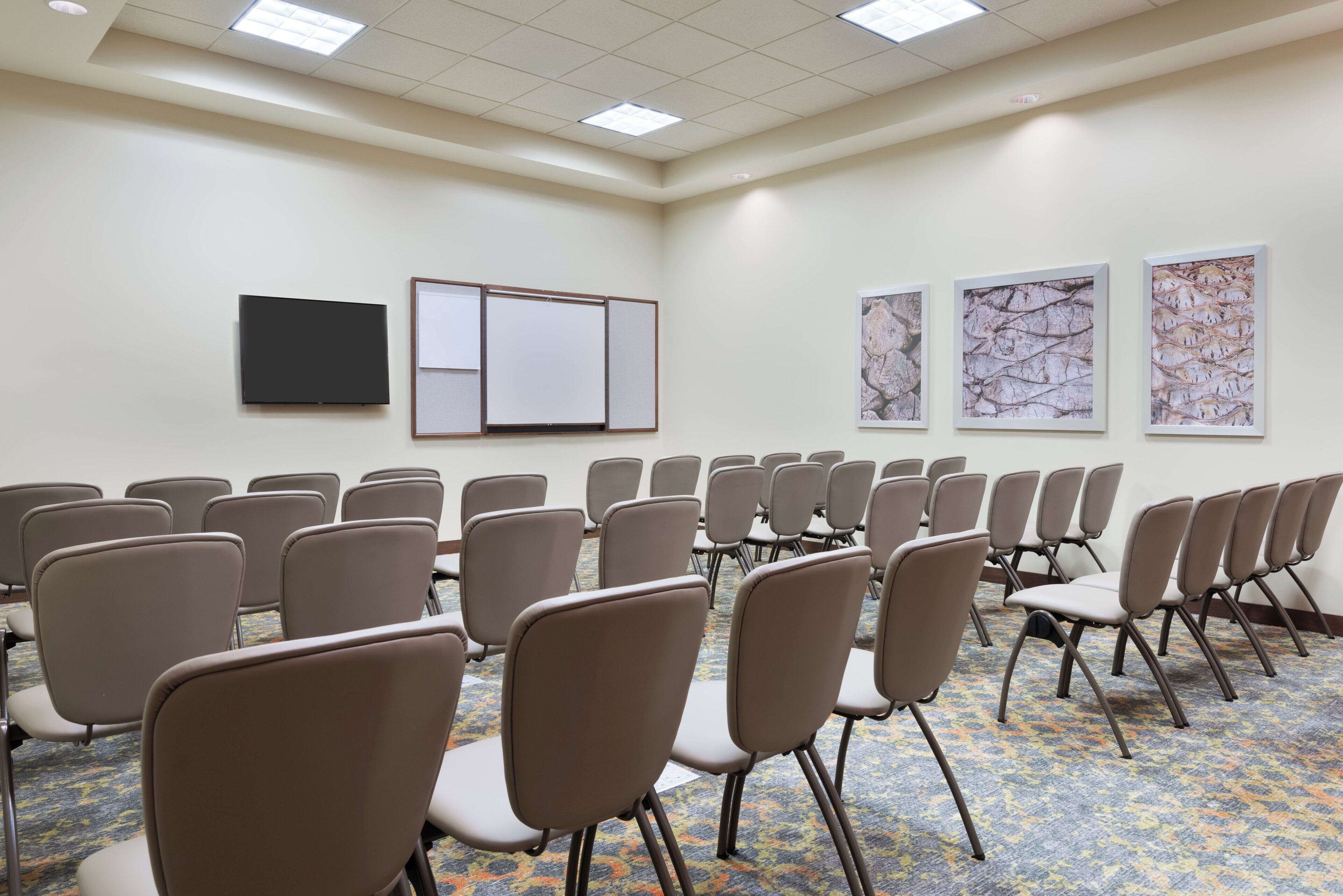 A conference room with rows of chairs, a whiteboard, a flat-screen TV, and abstract art on the walls.