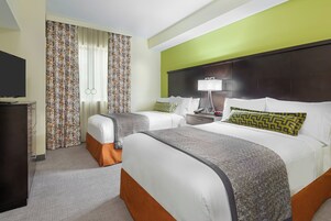 A hotel room with two beds, a desk, a TV, and a lamp.