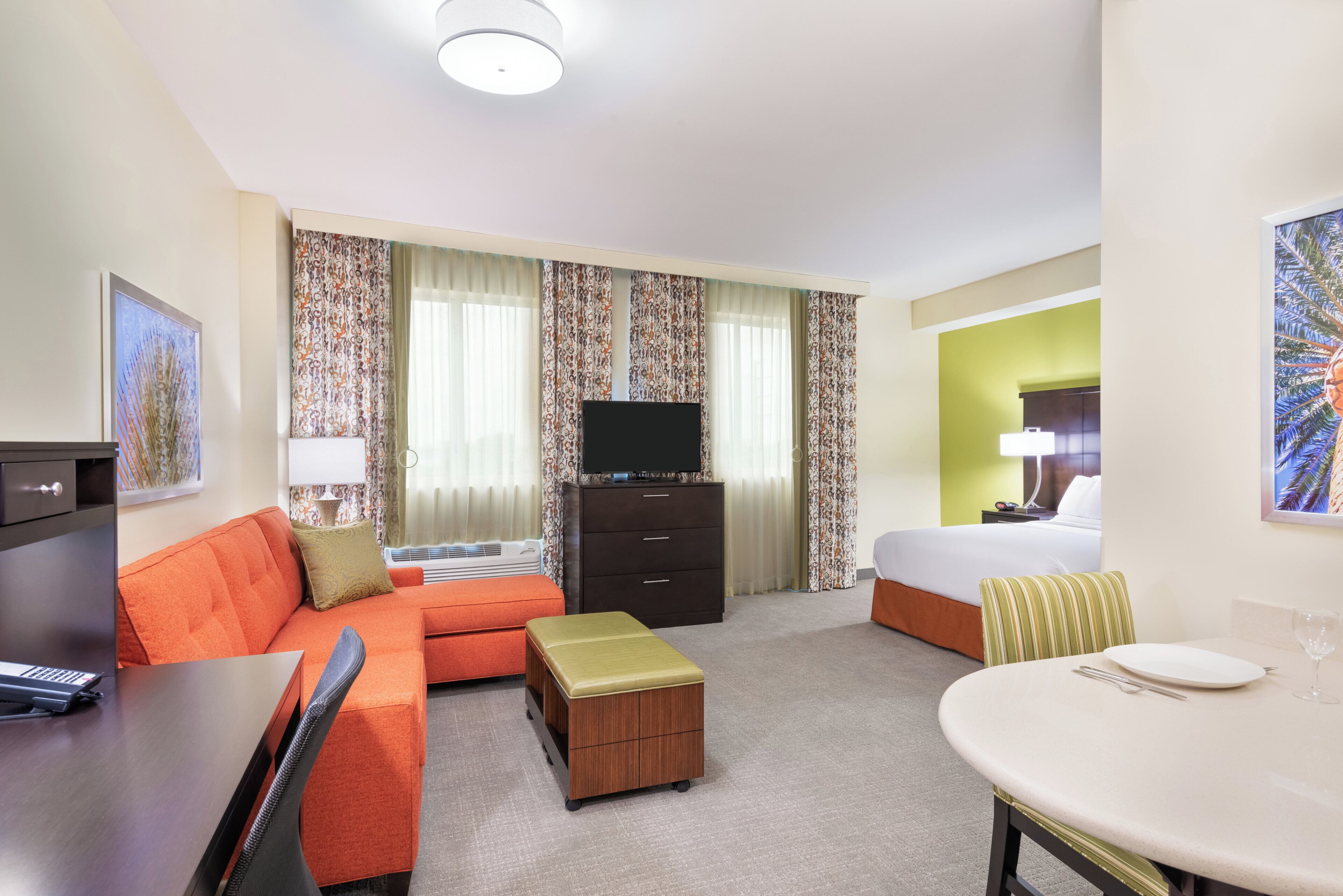 Ein Hotelzimmer mit einer Couch, einem kleinen Tisch, einem Fernseher, einem Bett und einem Schreibtisch mit Tastatur.