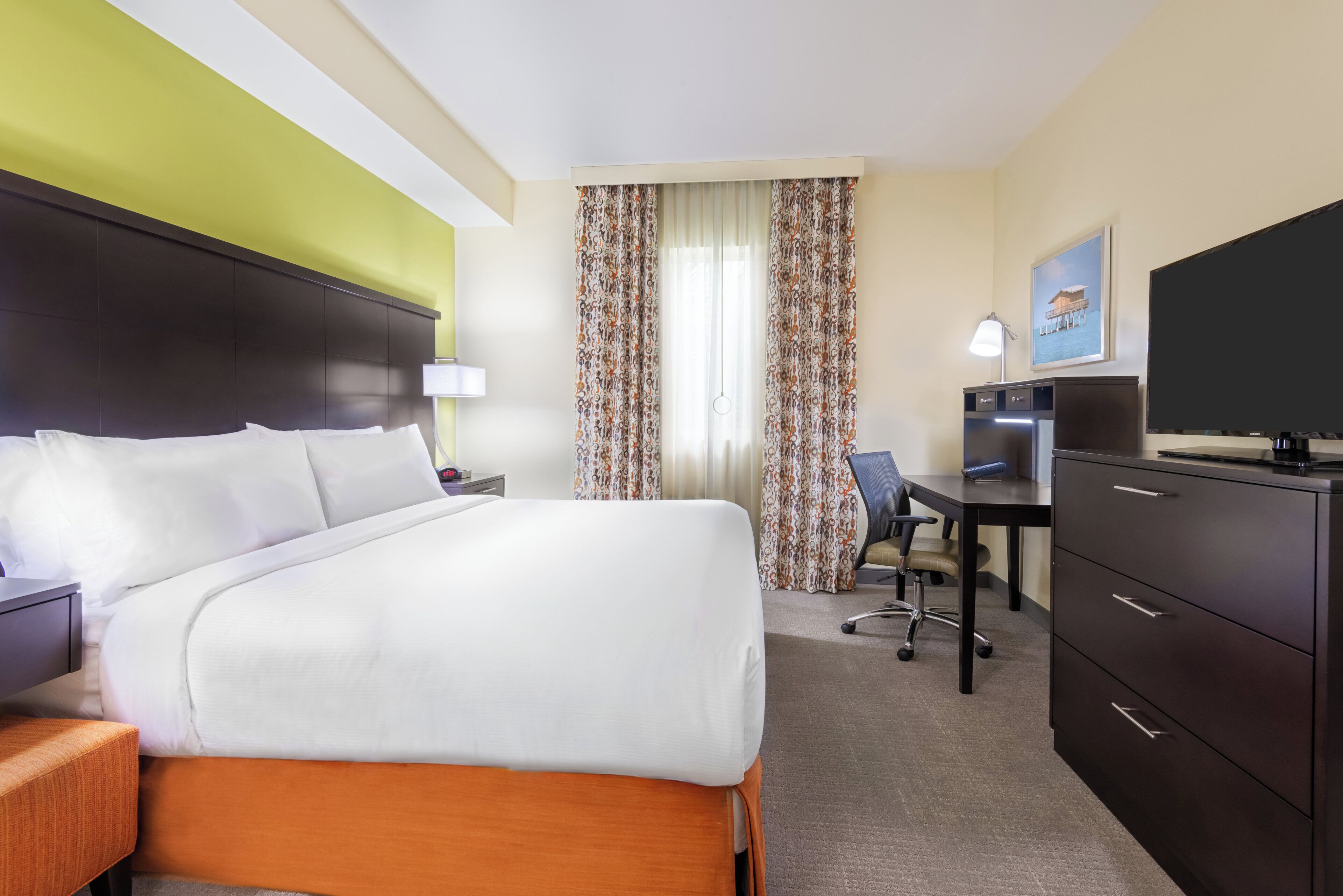 A hotel room with a bed, desk, chair, TV, and a desk lamp.