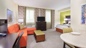 Habitación de hotel con sofá, una mesita, televisión, cama y escritorio con silla.