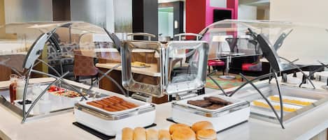 A buffet counter with various food items and a seating area with chairs.