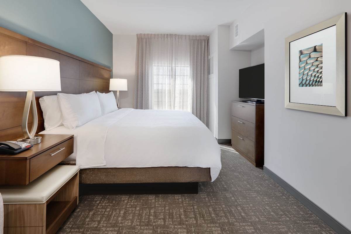 A hotel room with a bed, bedside tables, a TV, a desk, and a framed picture on the wall.