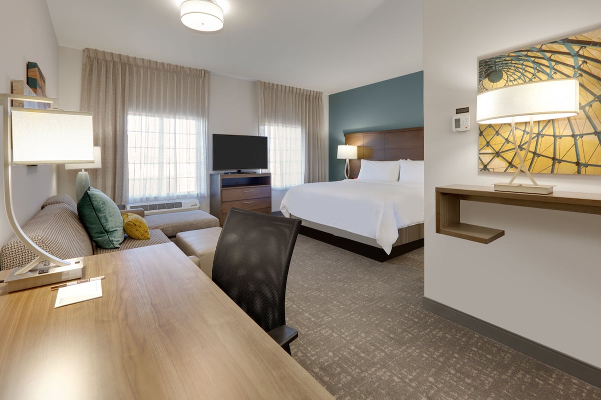 A hotel room with a bed, a desk with a lamp, a television, and a painting on the wall.