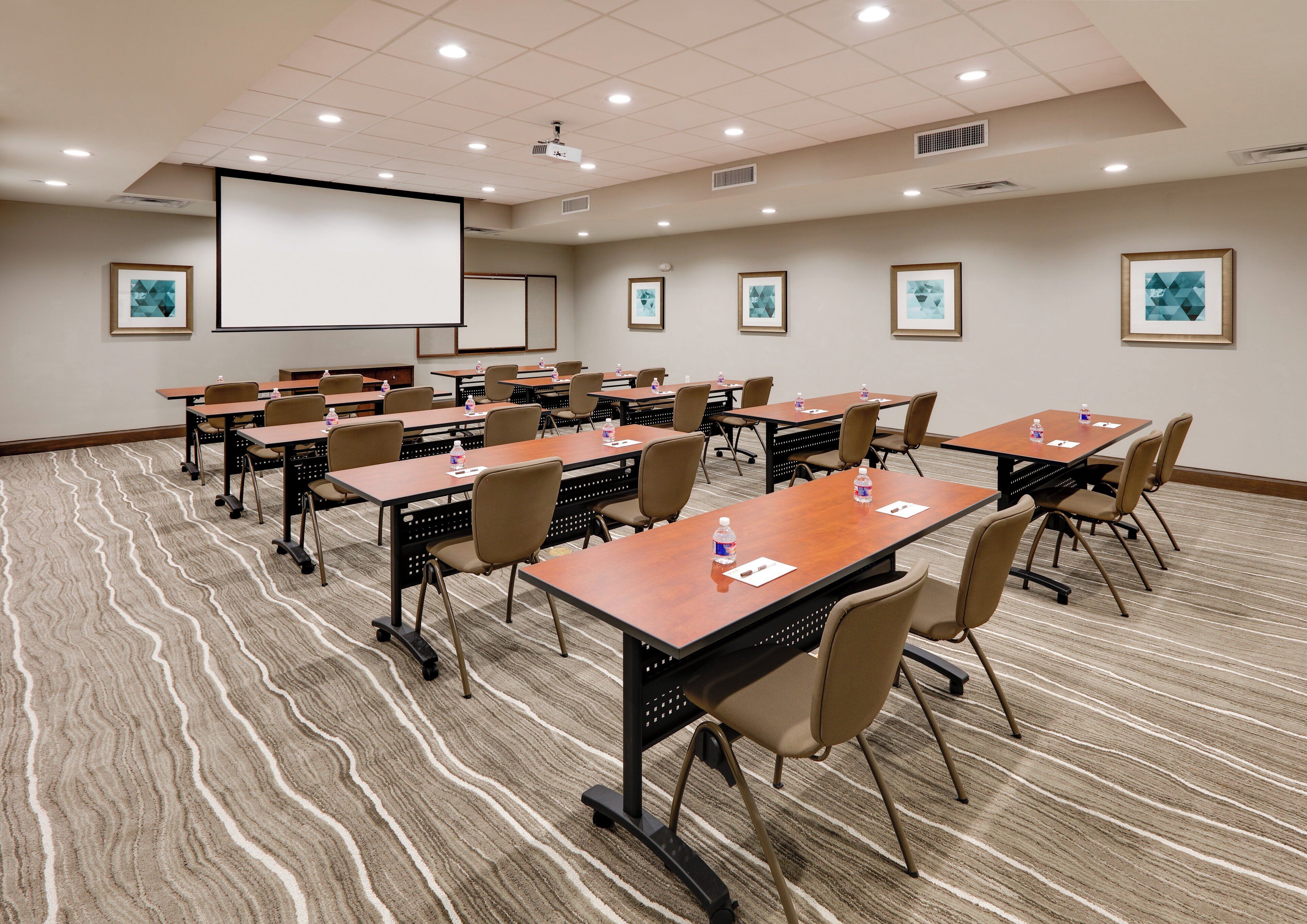 A conference room with multiple tables and chairs, equipped with projectors and screens, and framed artwork on the walls.