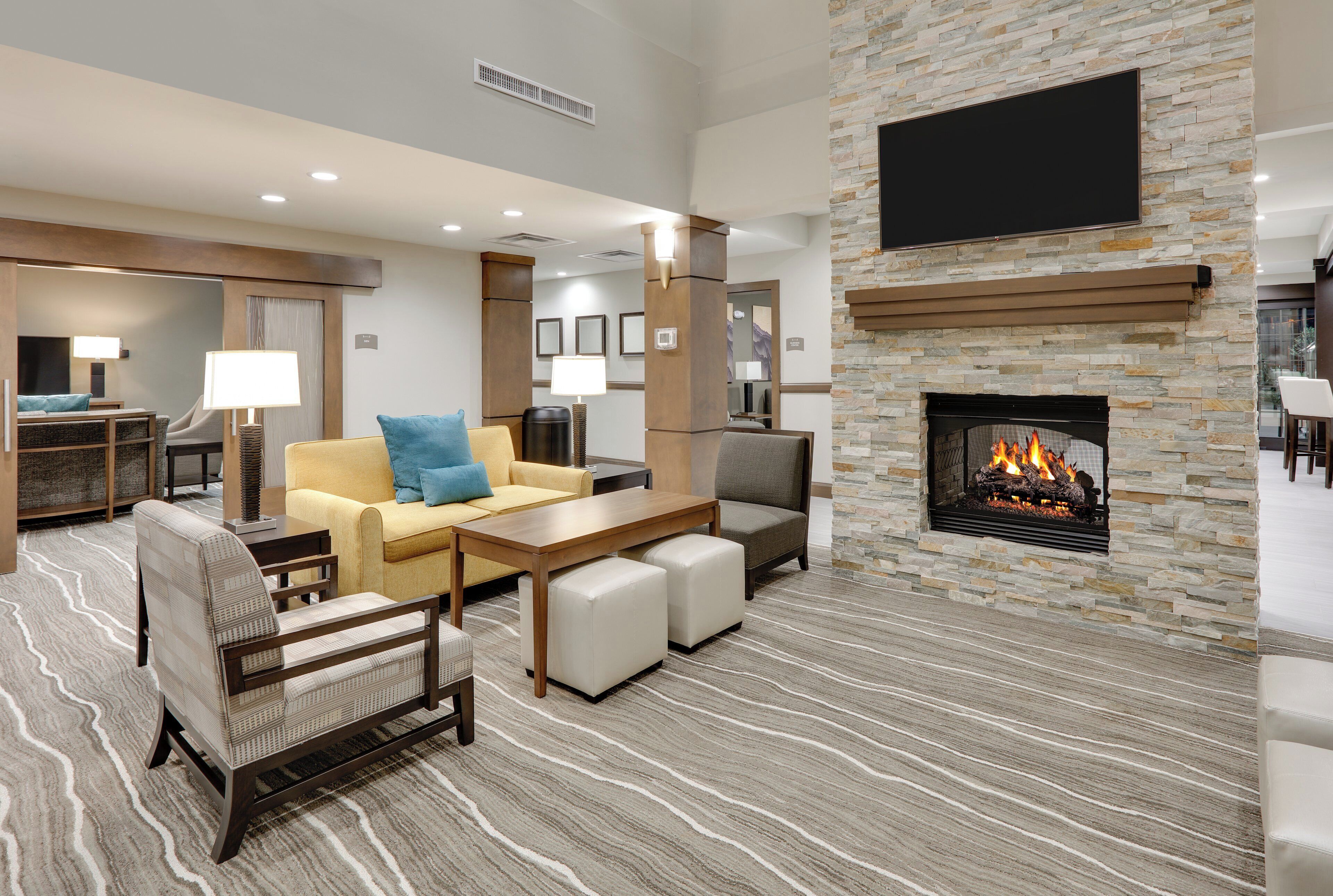 A hotel lobby with a stone fireplace, seating area, and a flat-screen TV mounted on the wall.