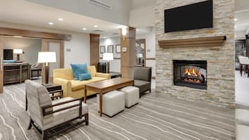 A hotel lobby with a stone fireplace, seating area, and a flat-screen TV mounted on the wall.