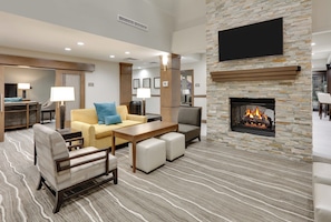 A hotel lobby with a stone fireplace, seating area, and a flat-screen TV mounted on the wall.