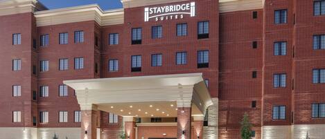 Un hotel Staybridge Suites con fachada de ladrillo, múltiples ventanas y un área de entrada cubierta.