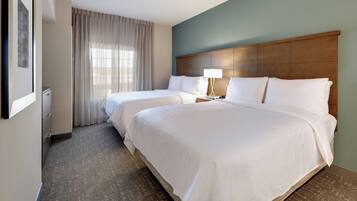A hotel room with two beds, a wooden headboard, a nightstand with a lamp, a window with curtains, and a framed picture on the wall.