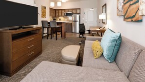 A compact living space with a flat-screen TV, wooden furniture, a kitchenette, and artwork on the walls.