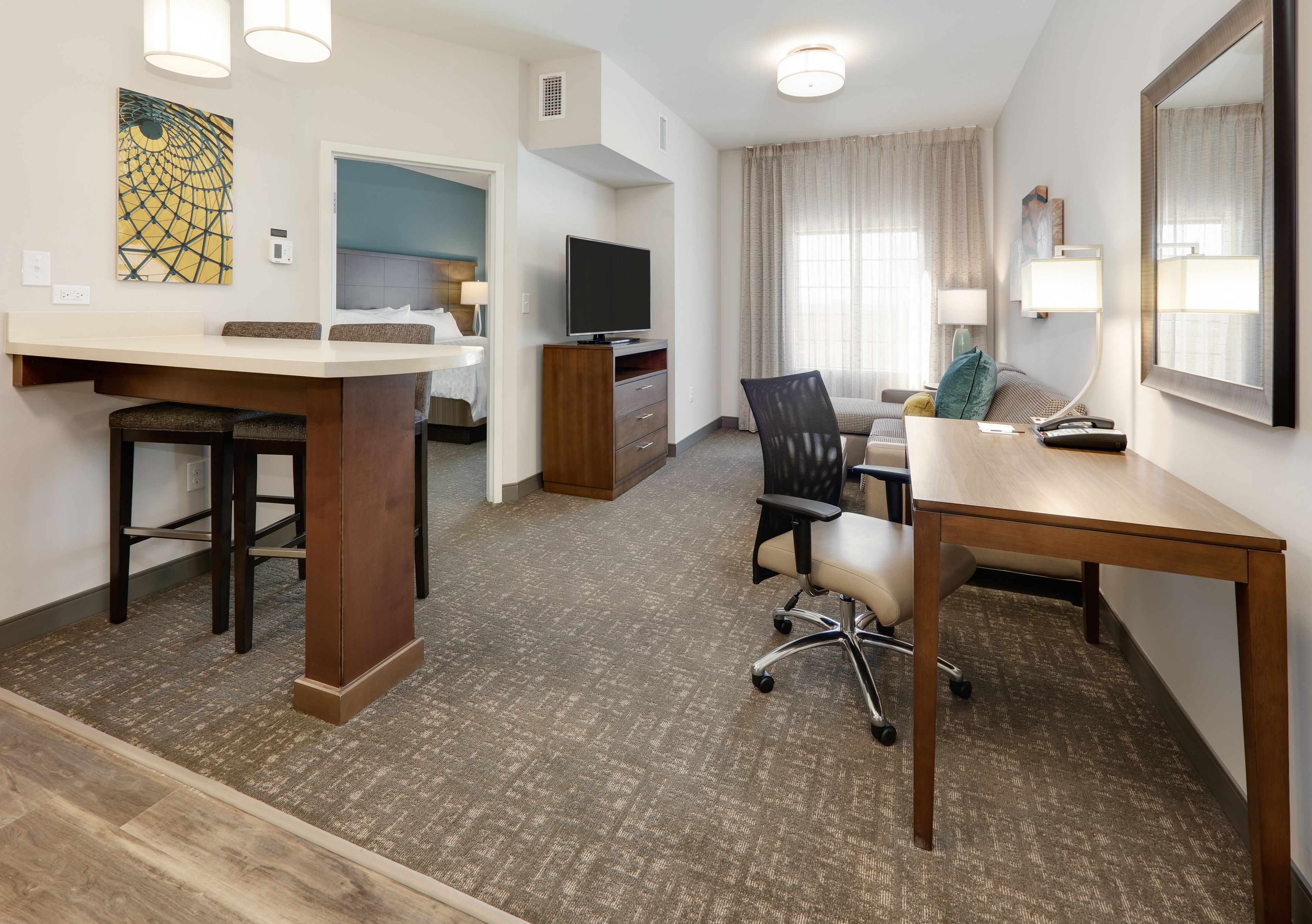Habitación de hotel con comedor, televisor, escritorio y un espejo grande.
