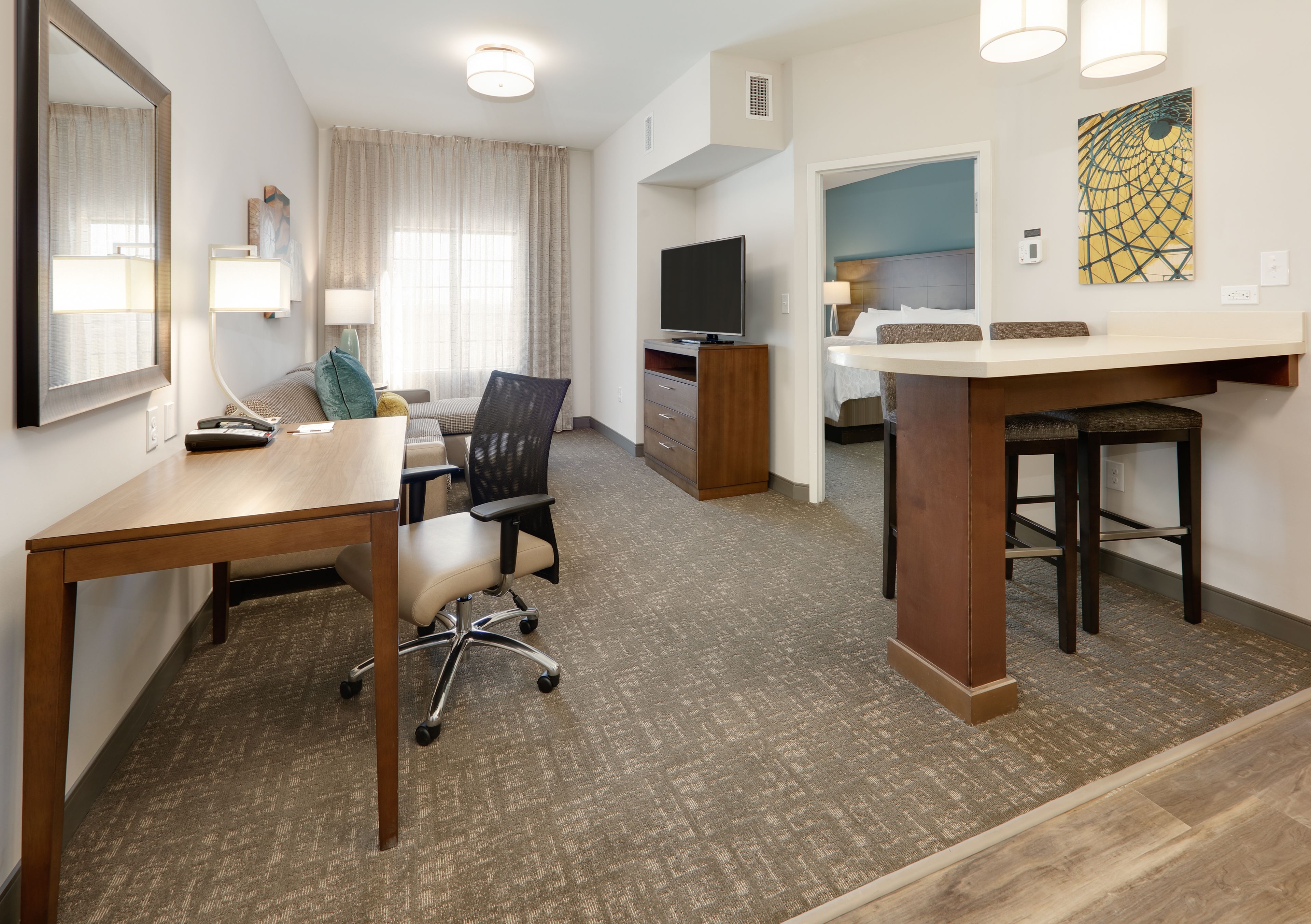 A hotel room with a desk, office chair, television, and a bed with a headboard.