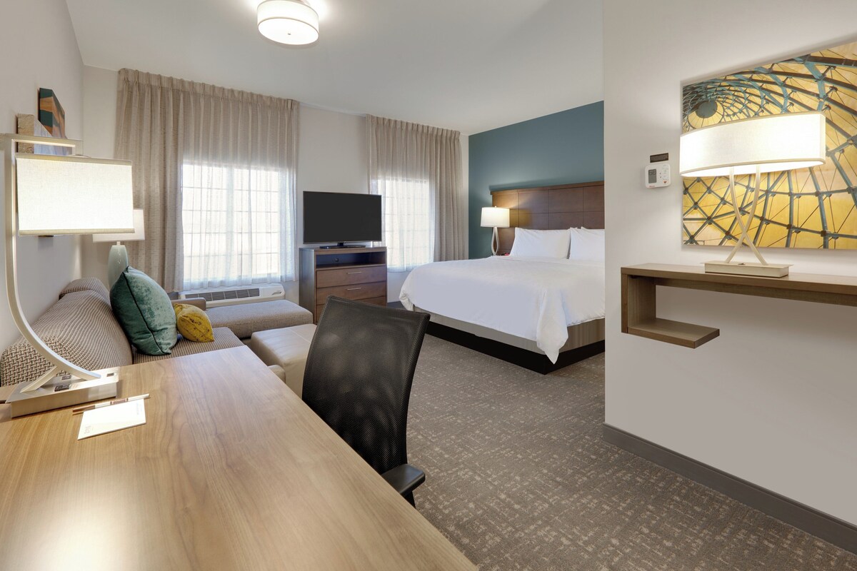 A hotel room with a bed, a desk, a television, a lamp, and a painting on the wall.
