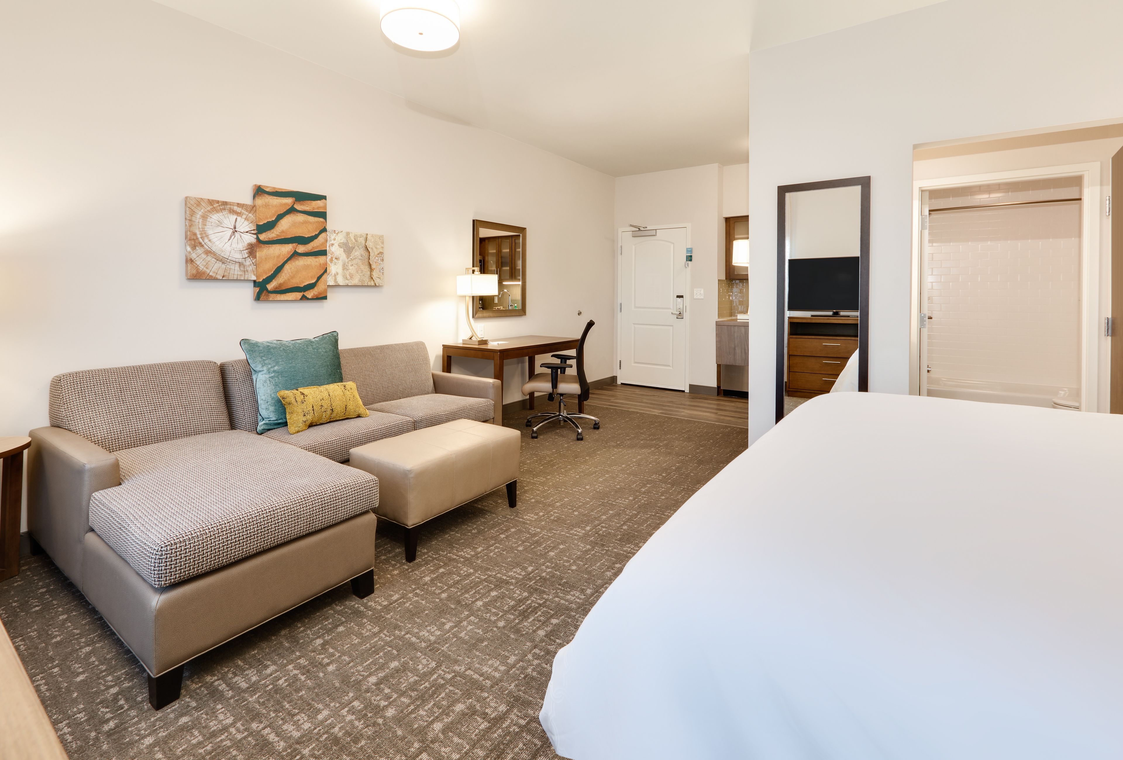 Een hotelkamer met een bed, een slaapbank, een bureau en een stoel. Er is een spiegel aan de muur en een deur naar de badkamer.