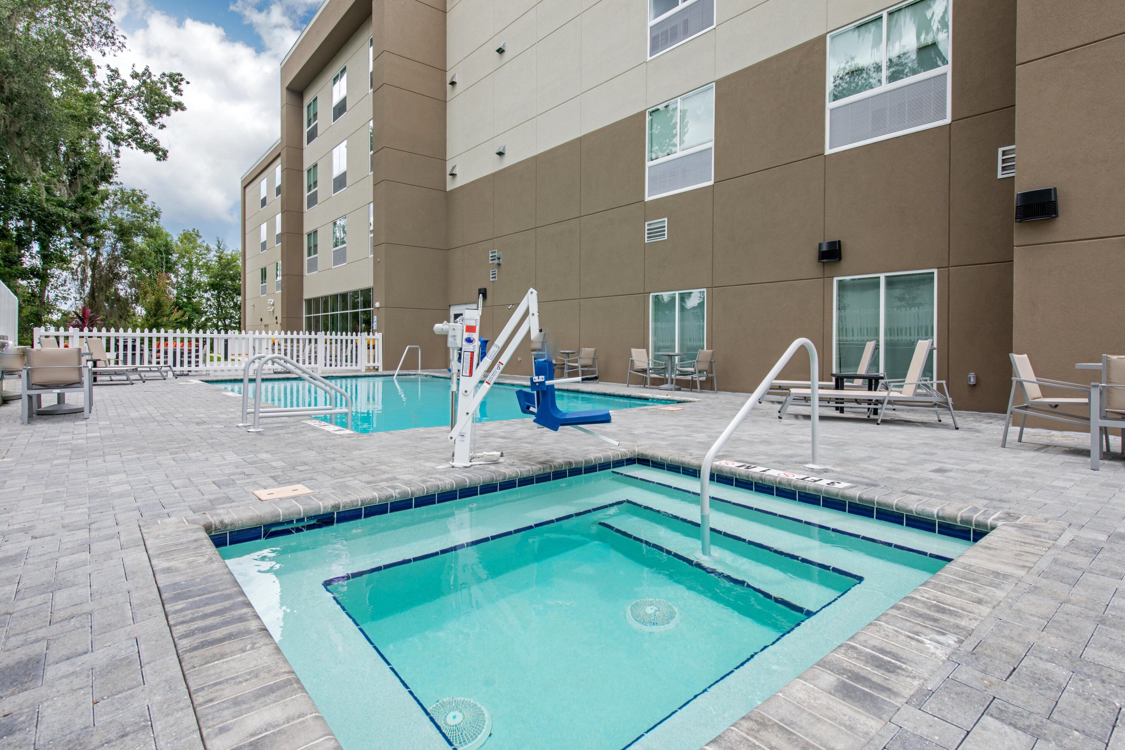 An outdoor swimming pool with a lifeguard stand, lounge chairs, and a white picket fence.