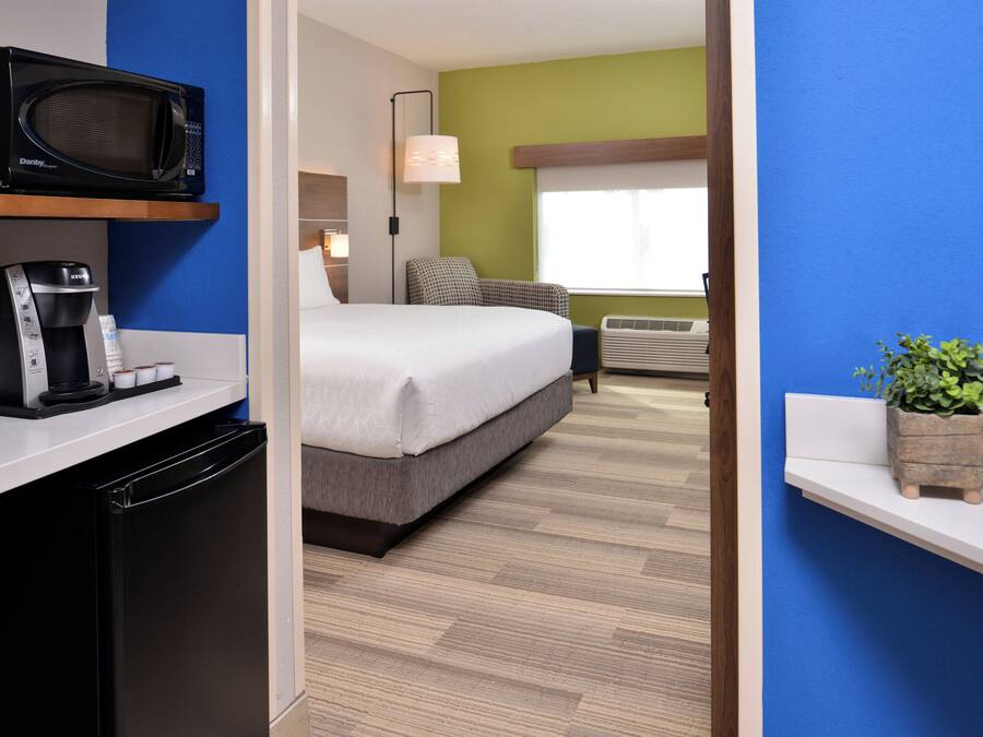 Een hotelkamer met een bed, een magnetron, een koffiezetapparaat, een lamp en een kleine plant.