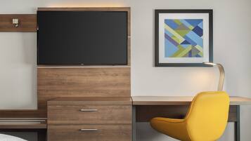 A modern hotel room with a wooden desk, a yellow chair, a flat-screen TV, and a framed abstract art piece on the wall.