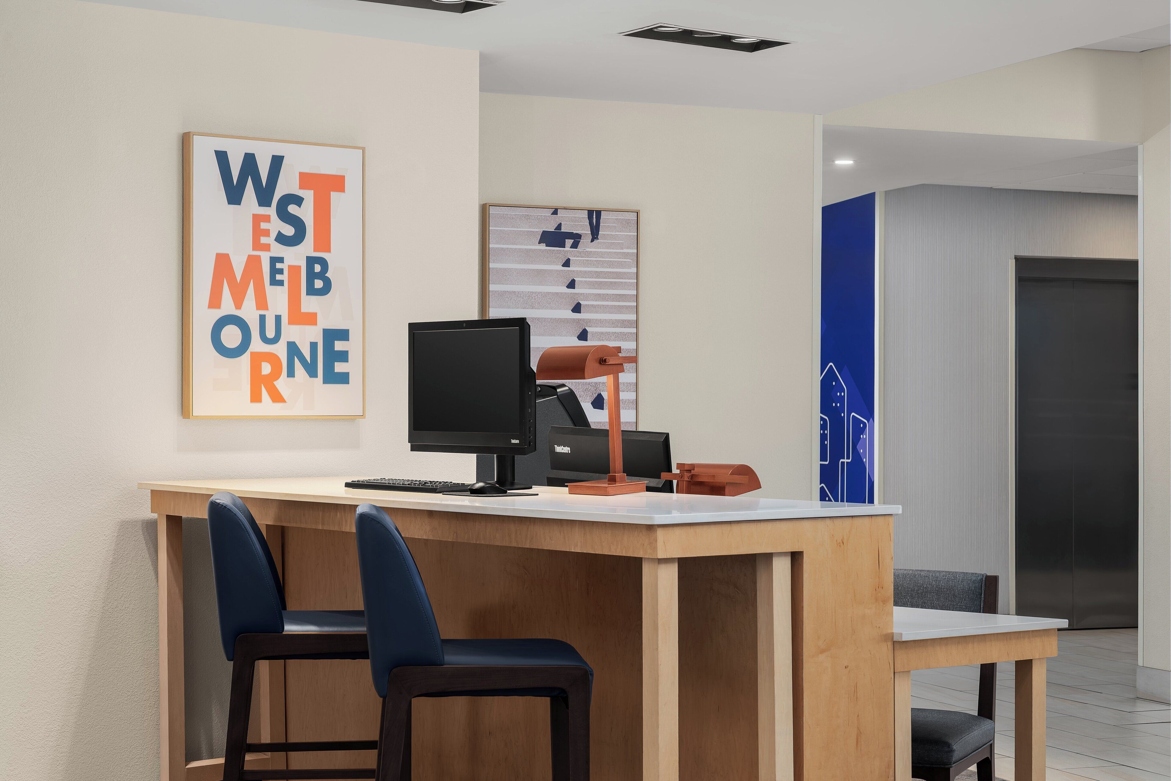 A modern office space with a desk, two chairs, a computer, and a framed artwork on the wall.