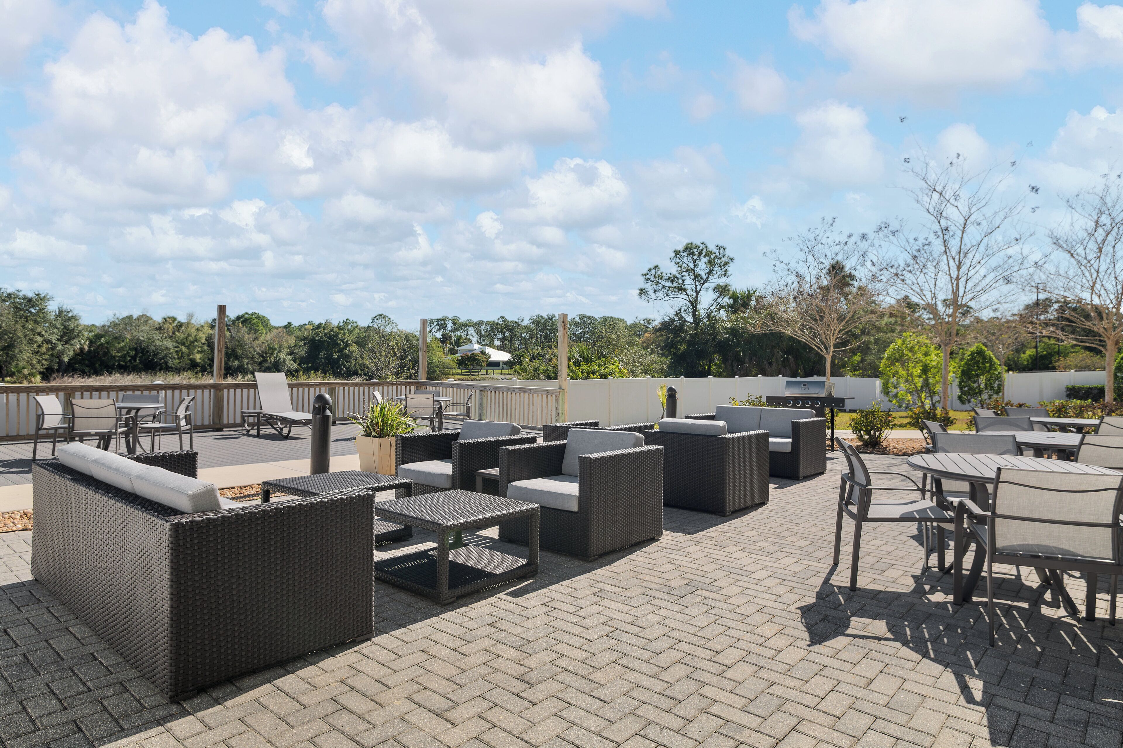 An outdoor patio area with wicker furniture, a barbecue grill, and a view of the surrounding trees and sky.