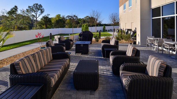 An outdoor patio with wicker furniture, a grill, and a view of a building and trees.