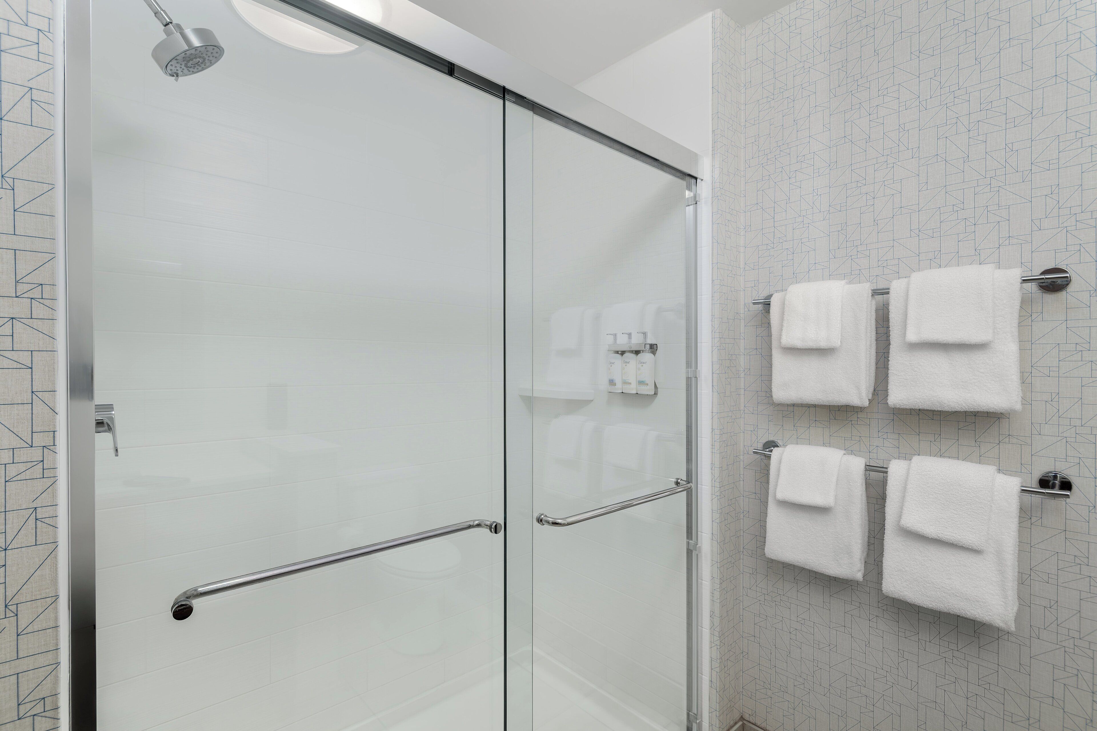 A modern bathroom with a glass shower enclosure, a glass door, and a towel rack with four white towels.