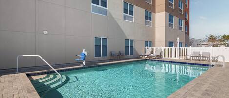 A swimming pool with a clear blue water, a white fence, and a building with multiple windows in the background.