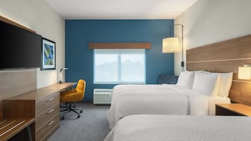 A hotel room with a desk, two beds, a chair, a TV, and a window with a view.