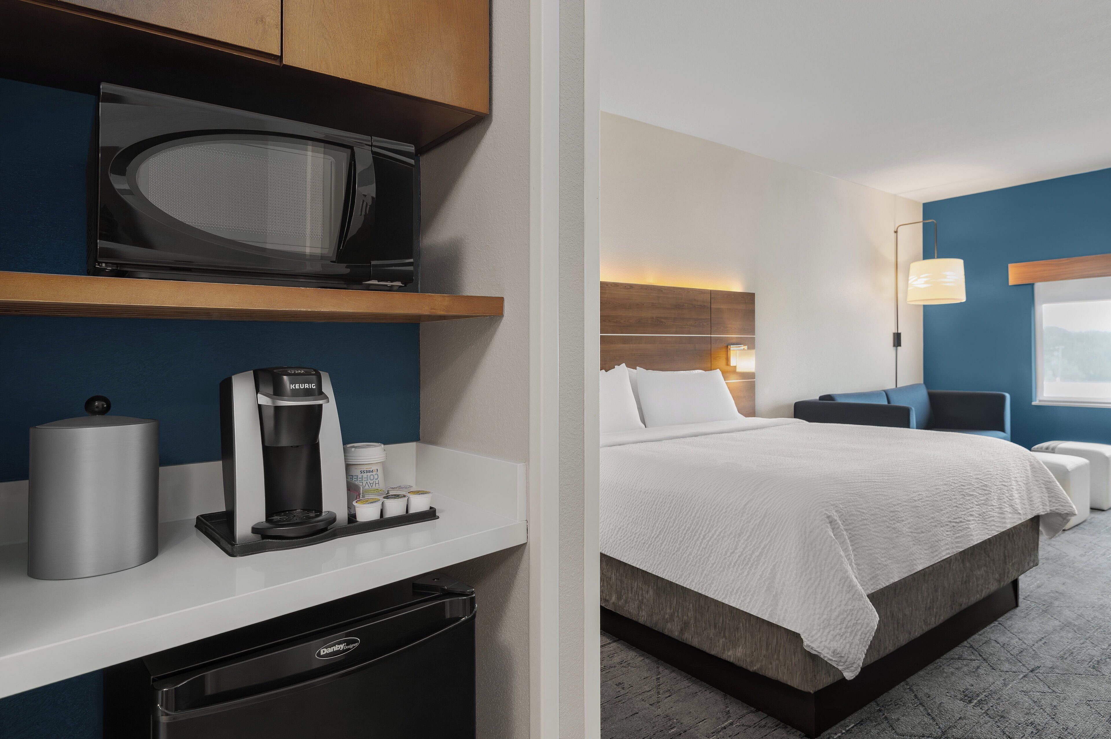 Hotellihuone, jossa on sänky, yöpöytä, lamppu ja kahvinkeitin tasolla.