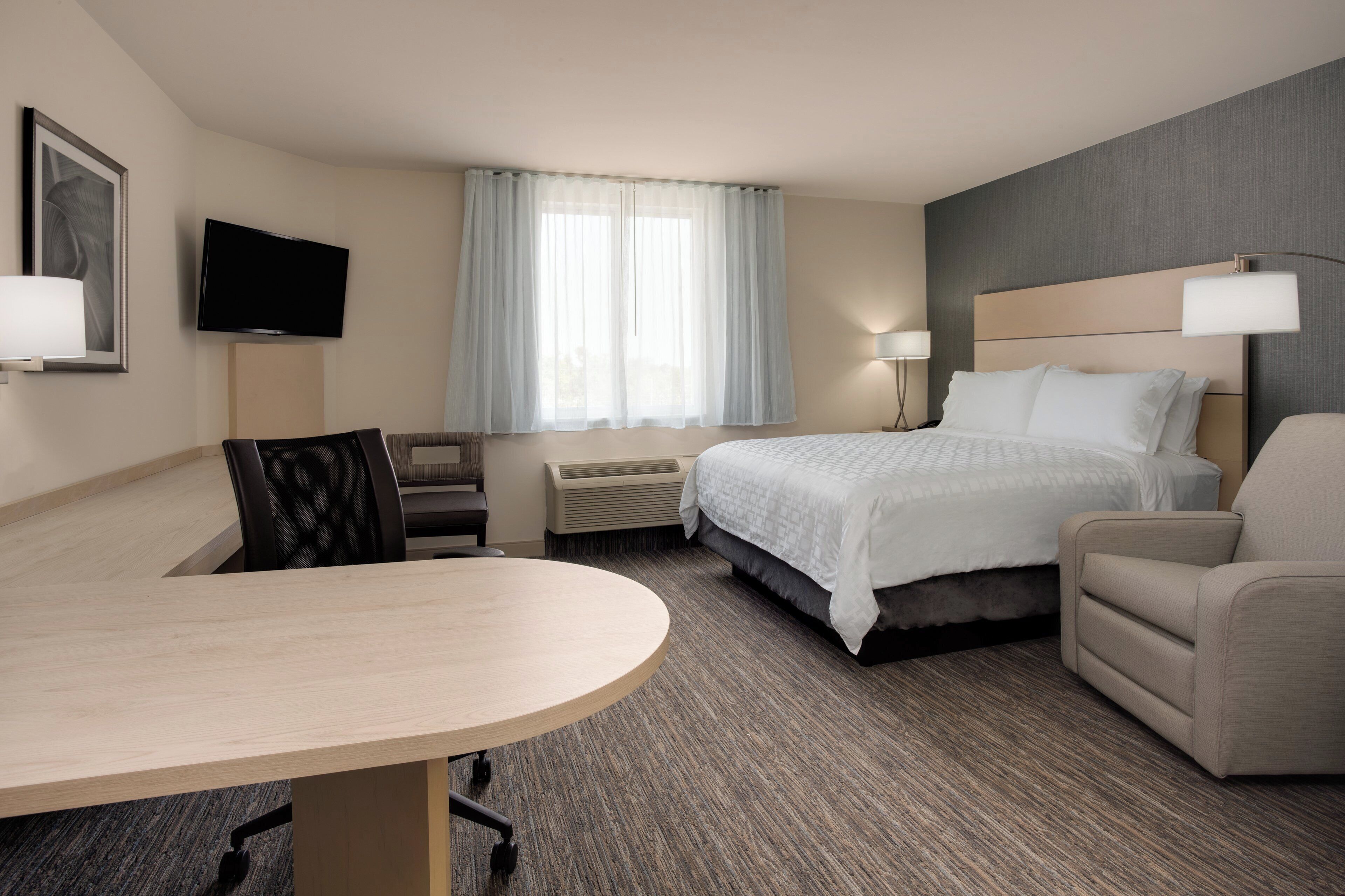 Een hotelkamer met een bed, een bureau, een stoel, een televisie en een raam met gordijnen.