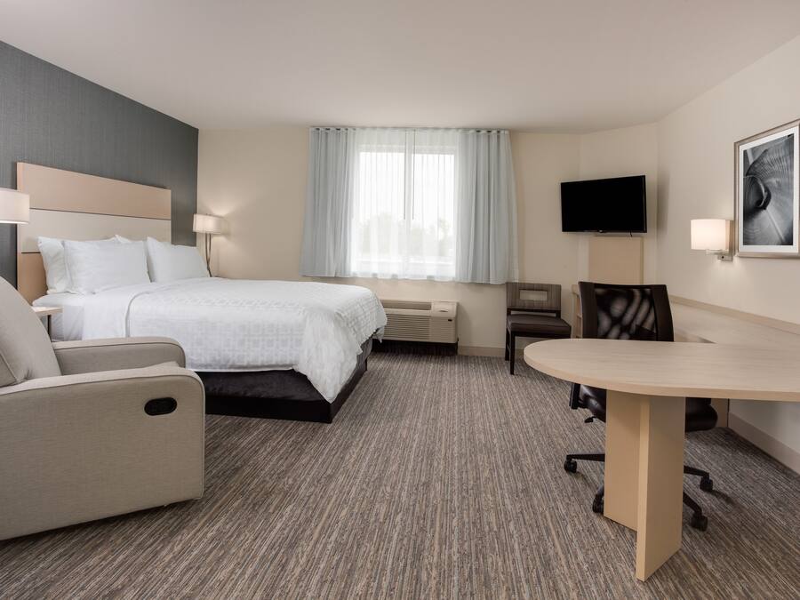 Une chambre d’hôtel avec un lit, un bureau, une chaise, une télévision et une fenêtre avec des rideaux.