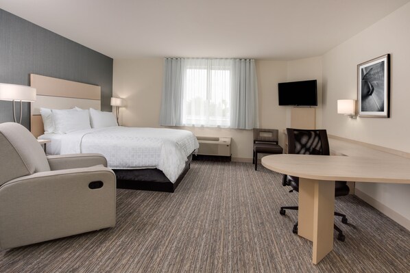 Habitación de hotel con cama, escritorio, silla, televisión y ventana con cortinas.