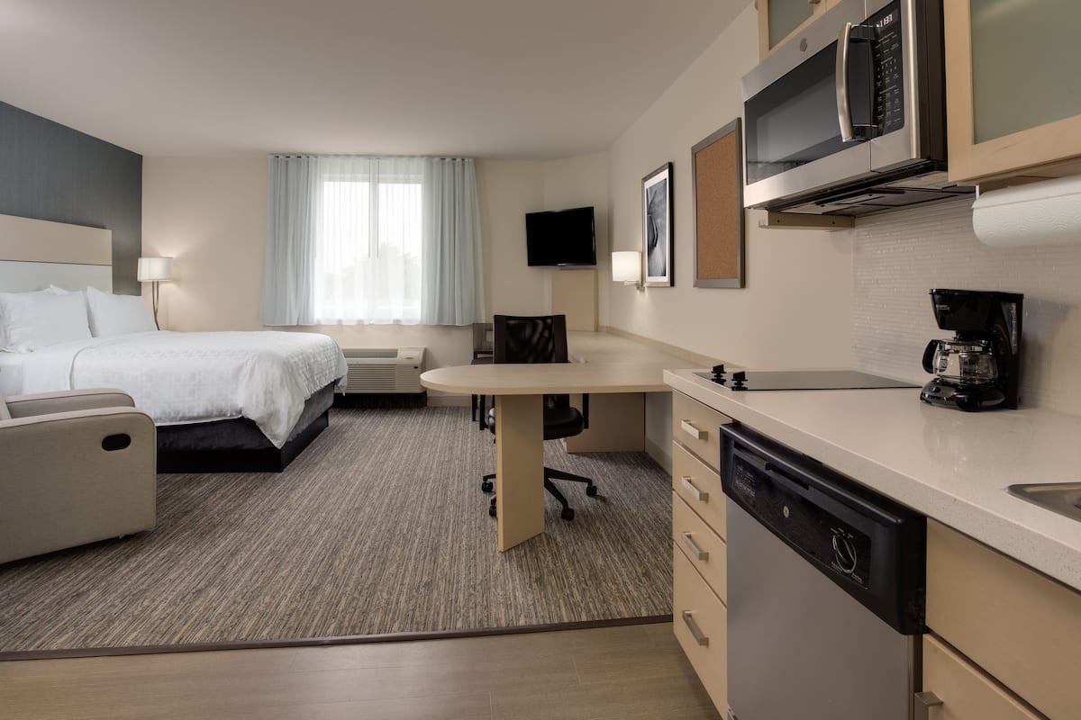 A hotel room with a bed, a desk, a chair, a television, a microwave, and a coffee maker.