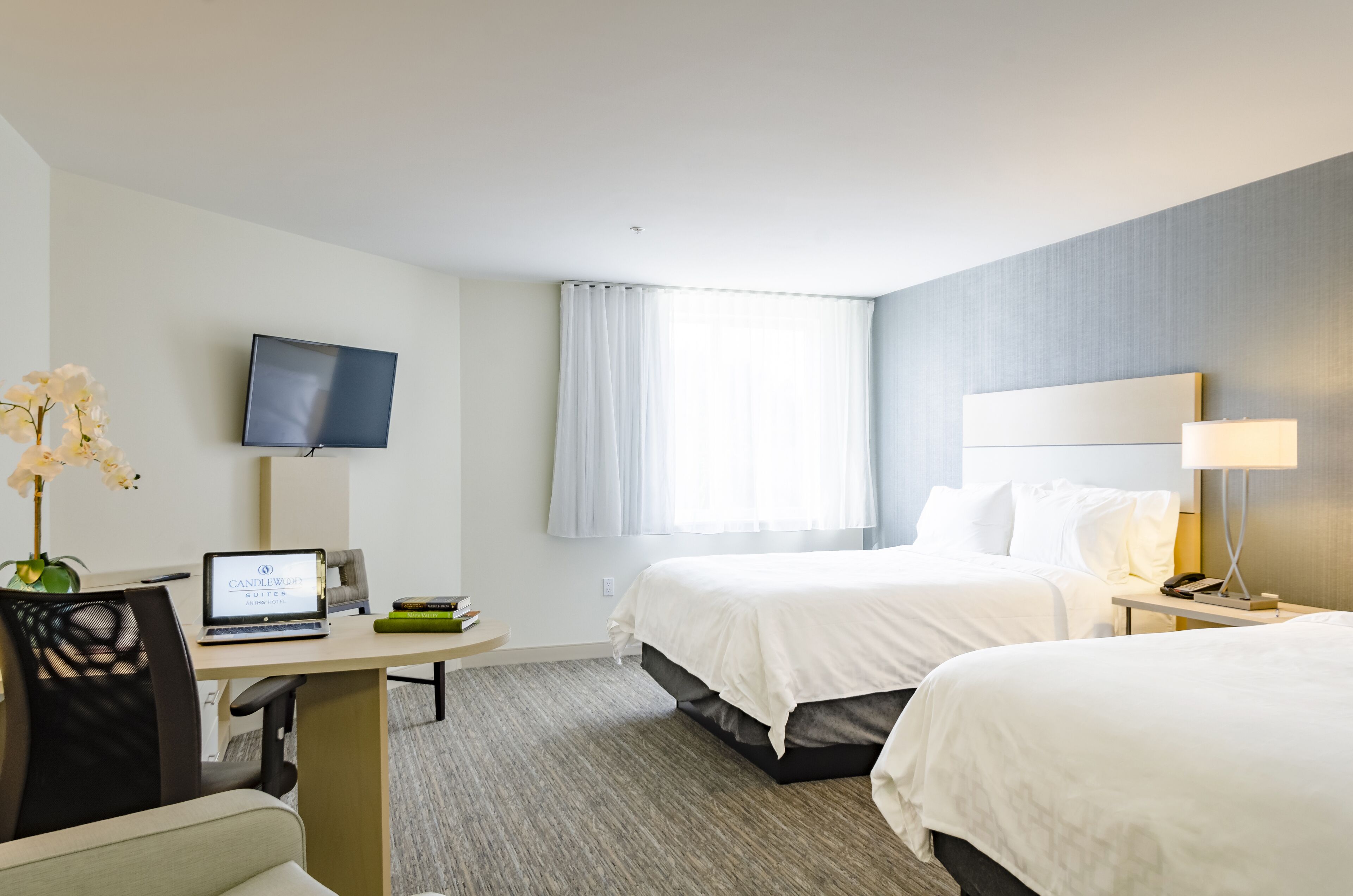 Une chambre d’hôtel équipée d’un bureau, de deux lits, d’une télévision et d’une fenêtre avec des rideaux.