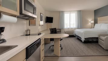 A hotel room with a kitchenette, a bed, a desk, and a TV.
